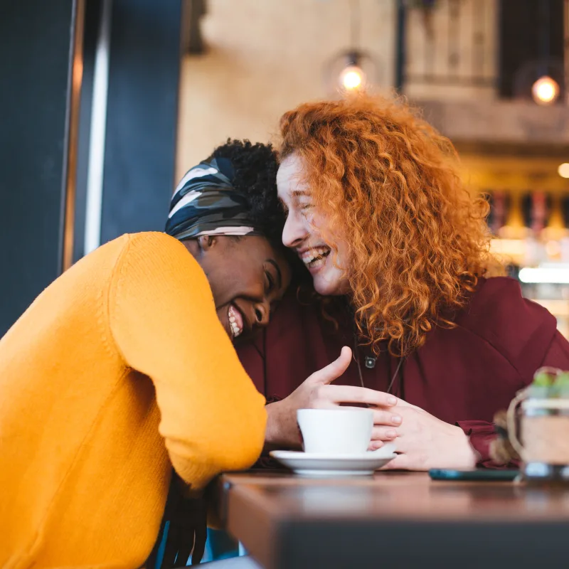 Business strategy - Two women at a coffee shop, their heads together, smiling