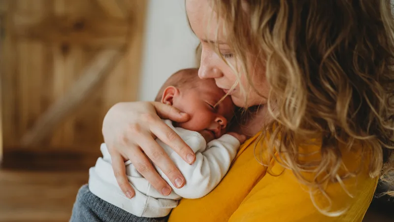 A blonde woman holds her small newborn baby to her chest