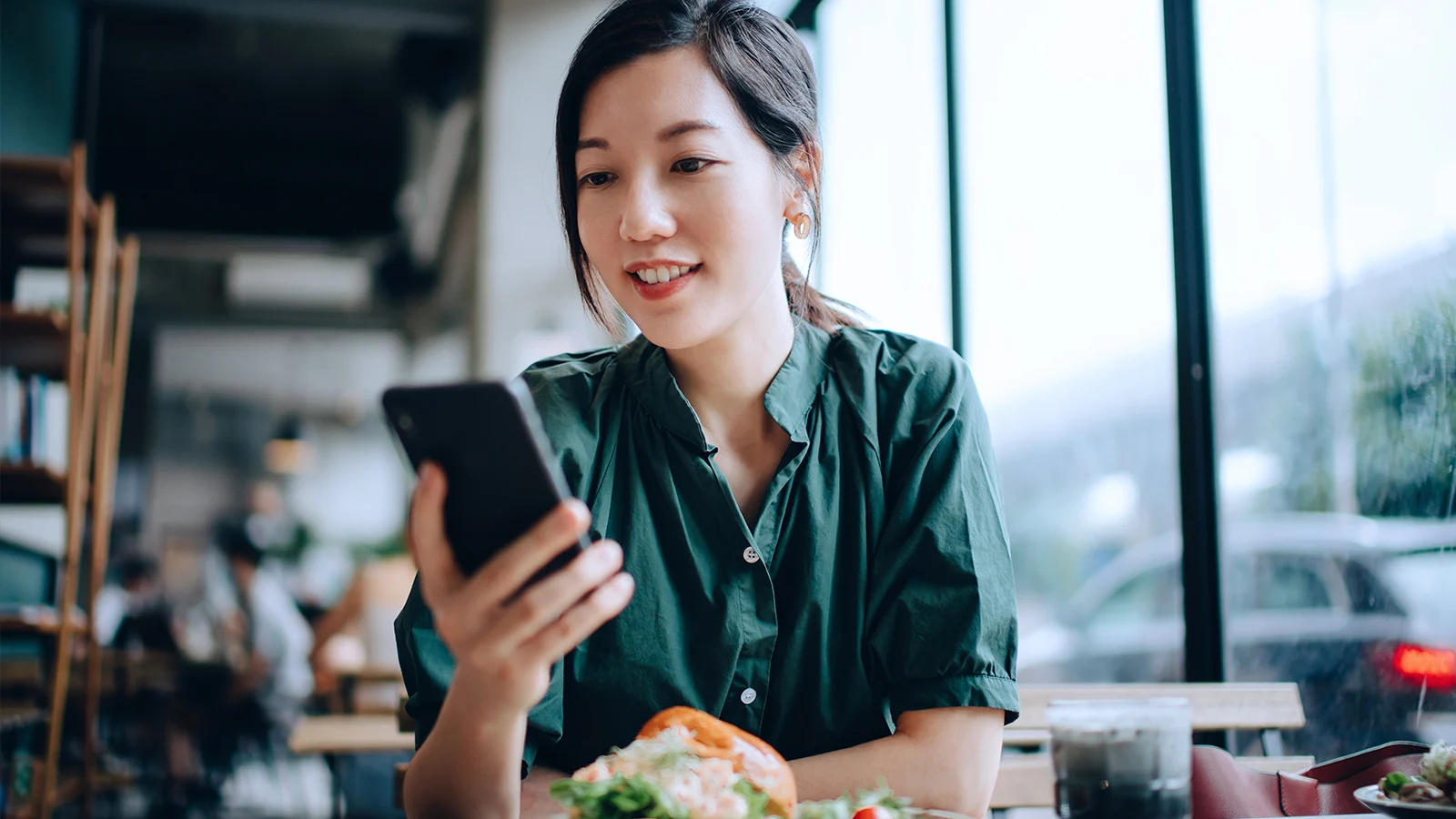 Young woman on smartphone while sitting in cafe having lunch