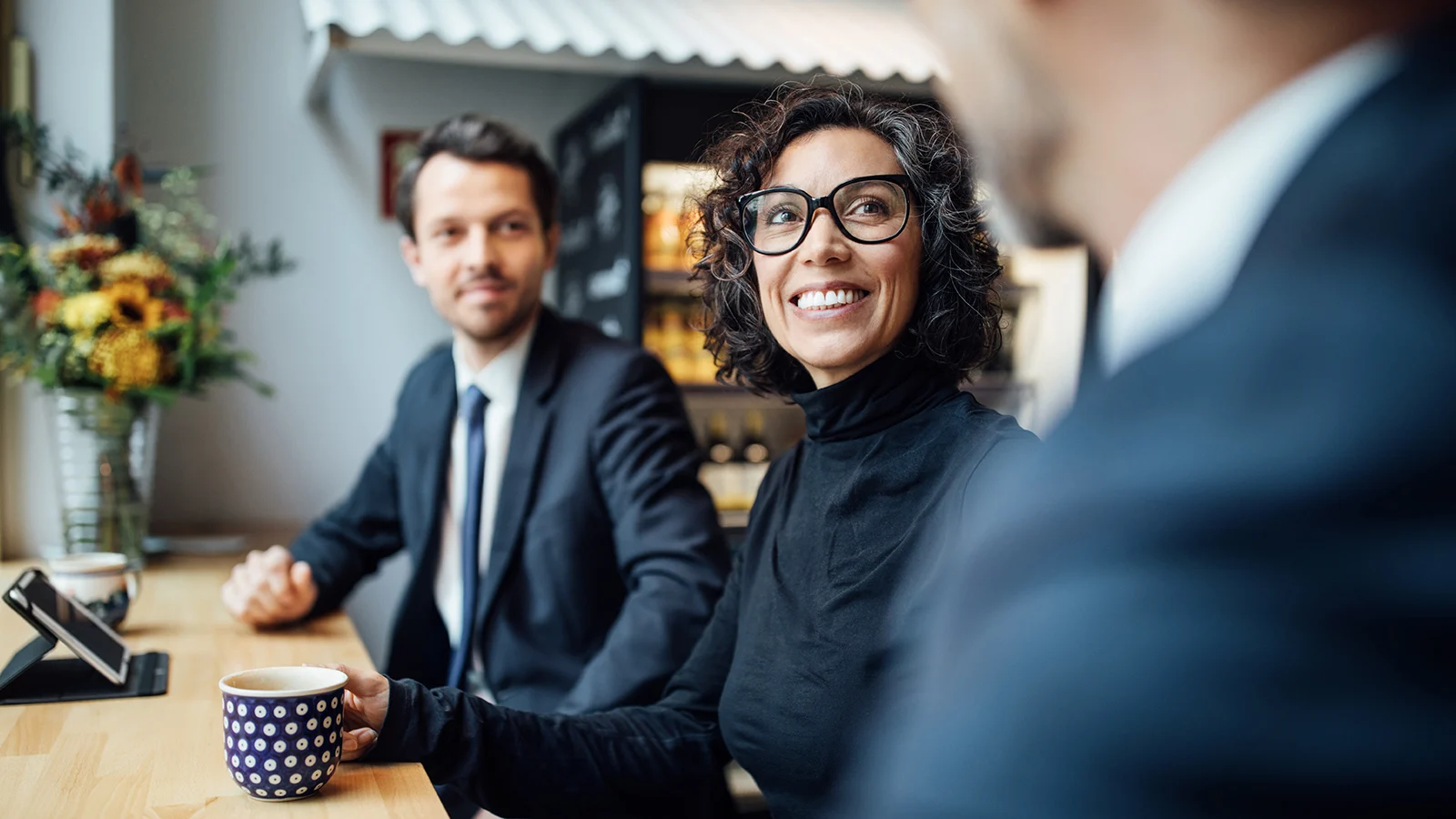 Three business people seated having coffee, woman in the middle is smiling