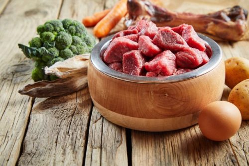 Raw dog food in wooden bowl surrounded by ingredients