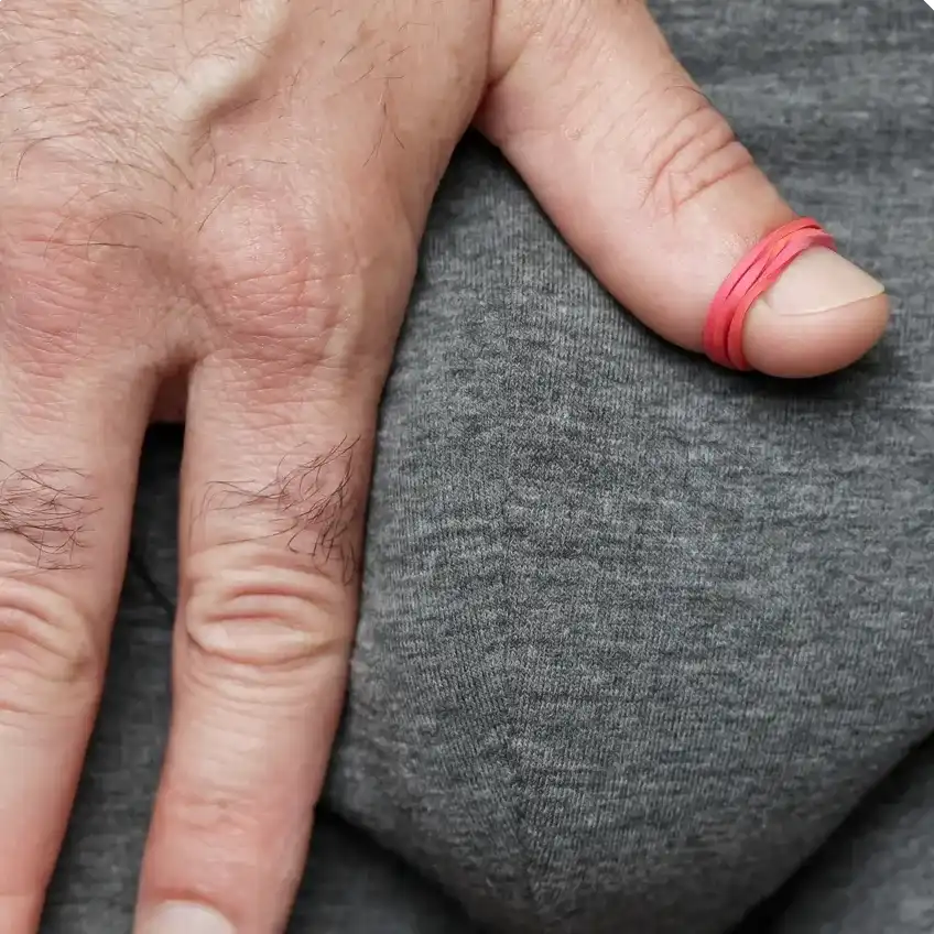 A man's hand since on his boxers while a rubber band is tied tightly around his thumb, to signify tight foreskin.