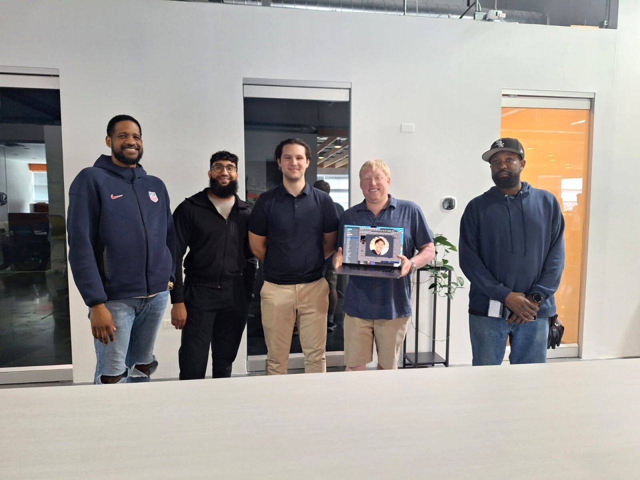 Company members standing together and one member is holding an open laptop.