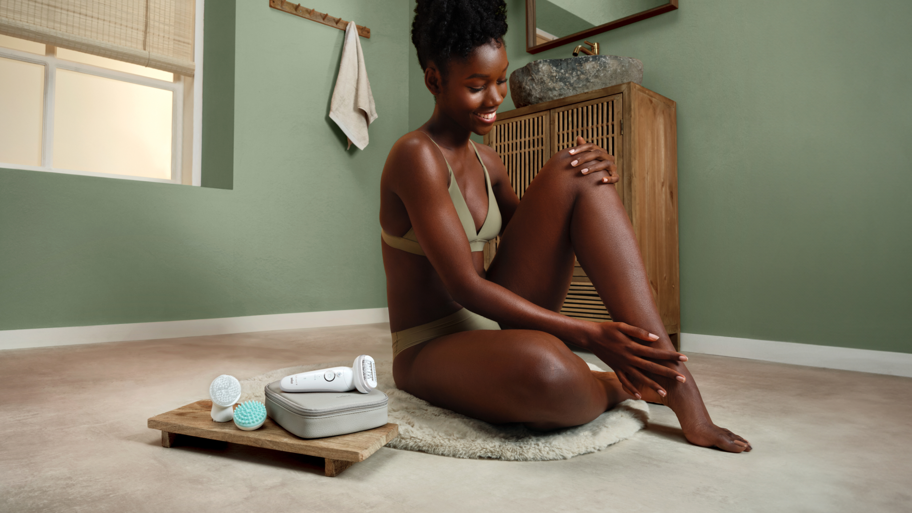 Woman sitting on the floor with the epilator and attachments plus pouch next to her.