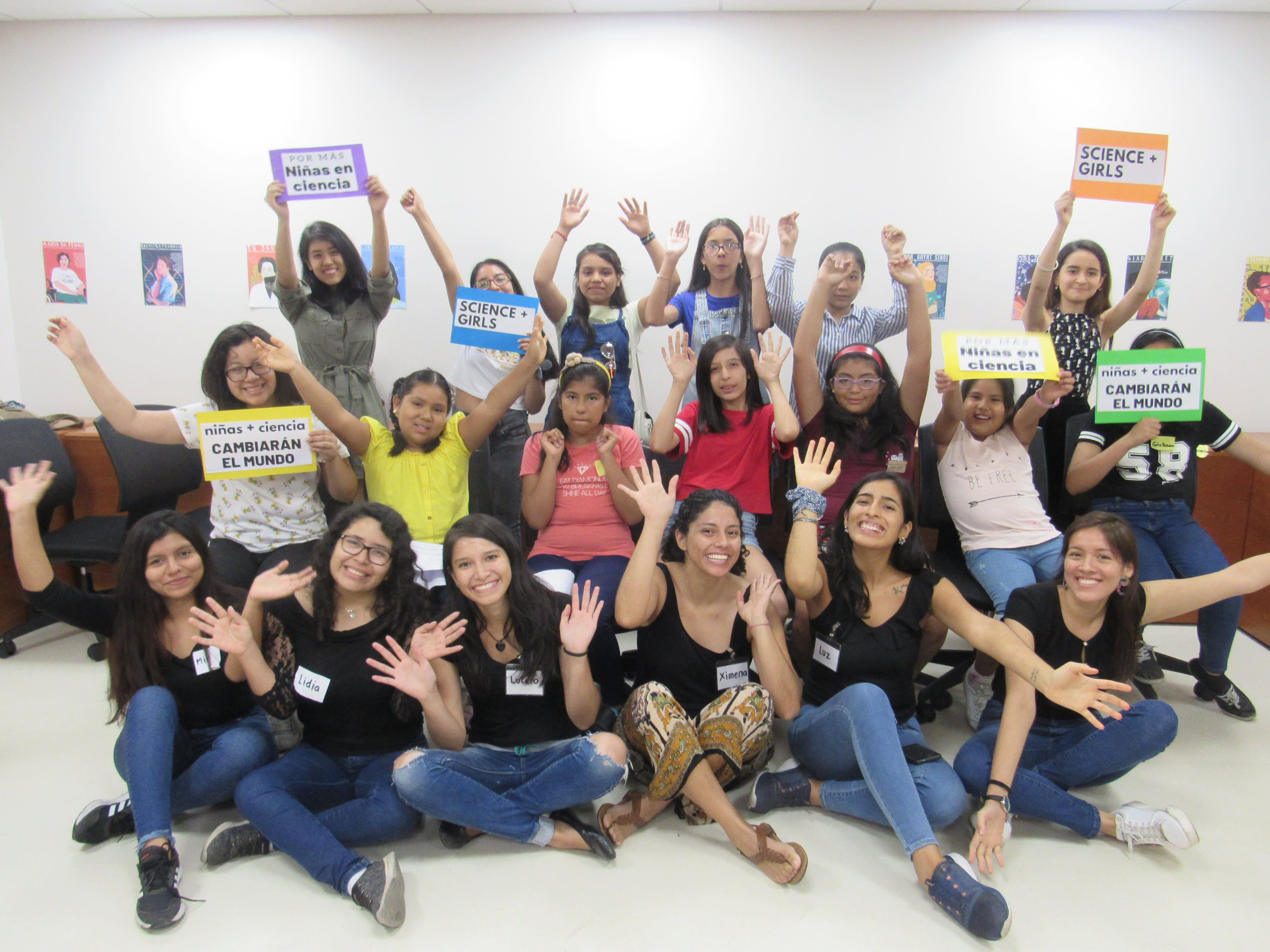 A group of young women, some sitting and some standing, with their hands in the air in celebration.