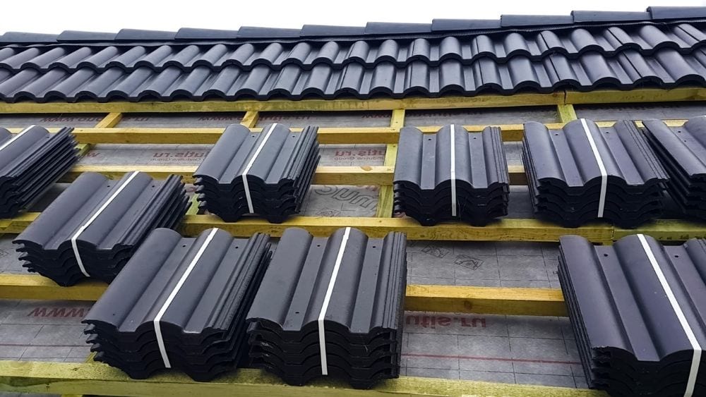 Black ceramic tiles being installed on a roof.