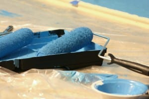 Image of a paint roller and paint tray next to a can of paint, on a drop cloth