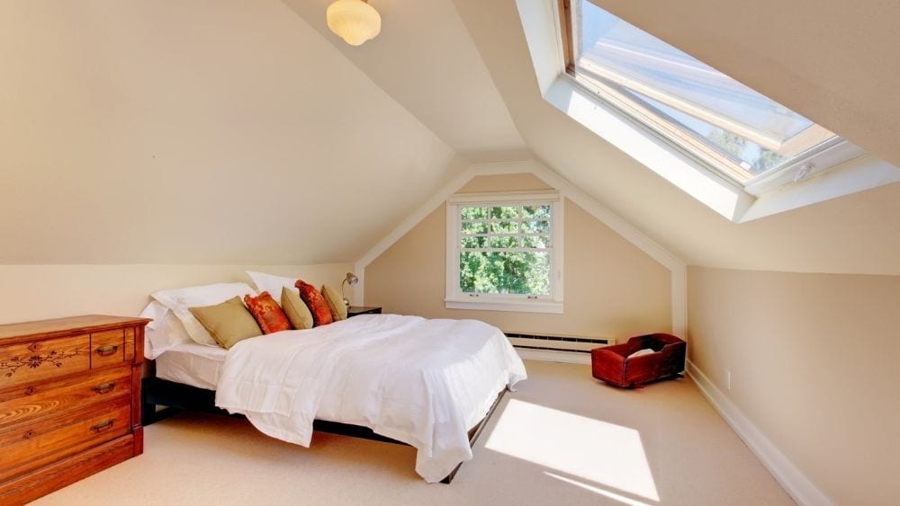 An attic bedroom with carpet floors and a skylight.