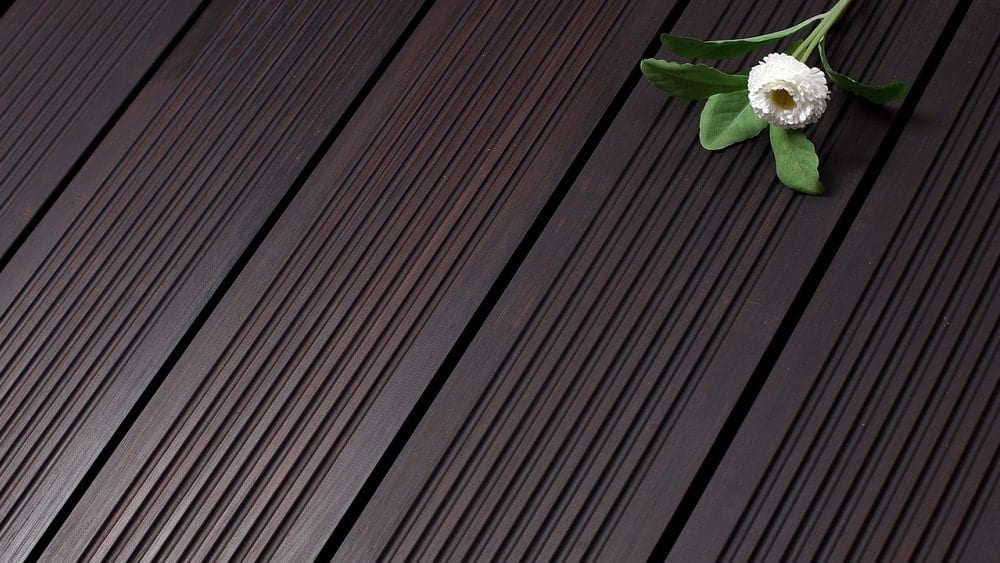 Close shot of dark bamboo flooring with a white flower laid on top.