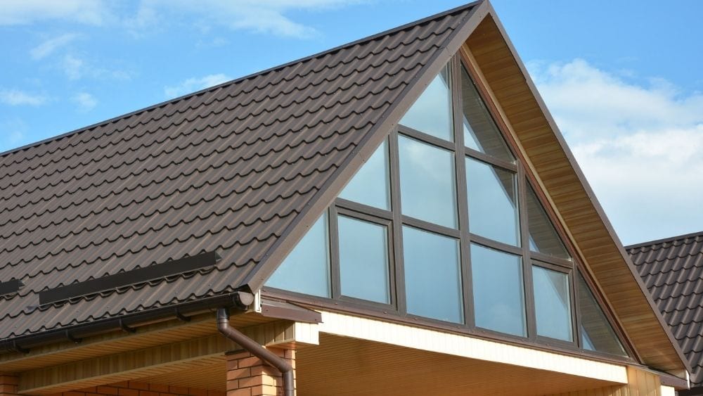 A modern house with lots of windows, in the peak of the roof, with a brown, corrugated metal roof on top. 