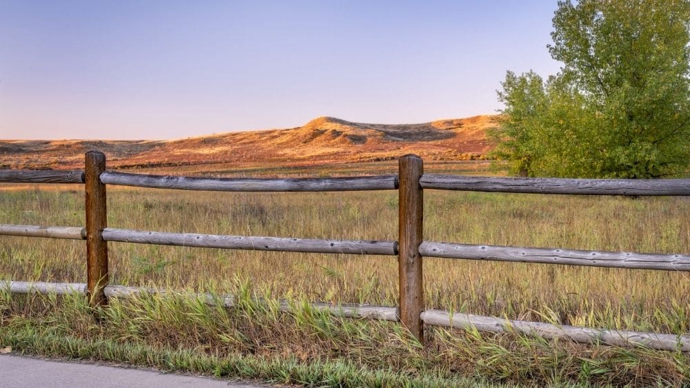 A wooden fence around an open field with a mountain range in the background.