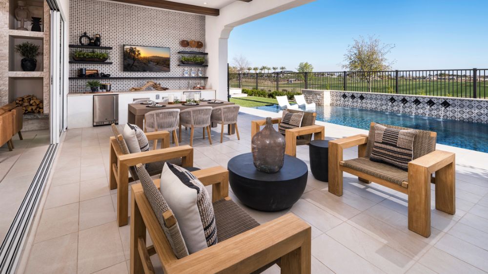 An outdoor living room. It has a TV, a sitting area and a dining area. It is beside a pool and separated from the house by large sliding doors.