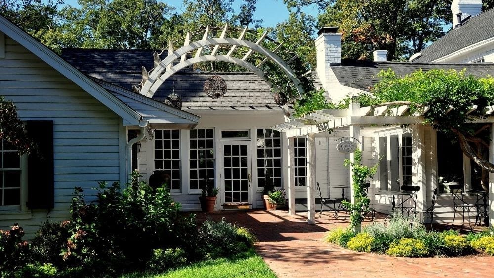 A brick courtyard between two white buildings with a wooden archway.