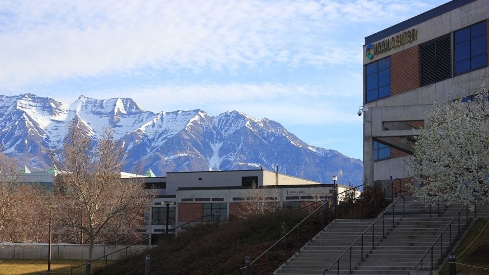An office building set against snow-capped mountains on a cloudy day.