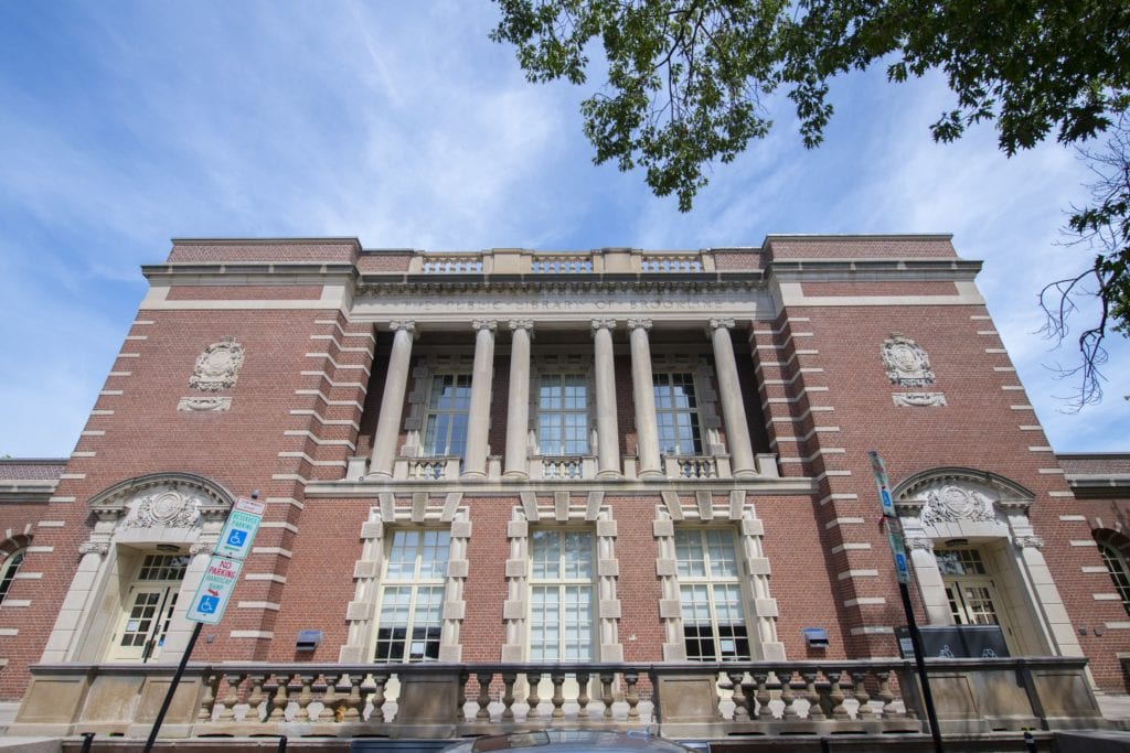 View from below of a red and white brick building with columns and large windows.