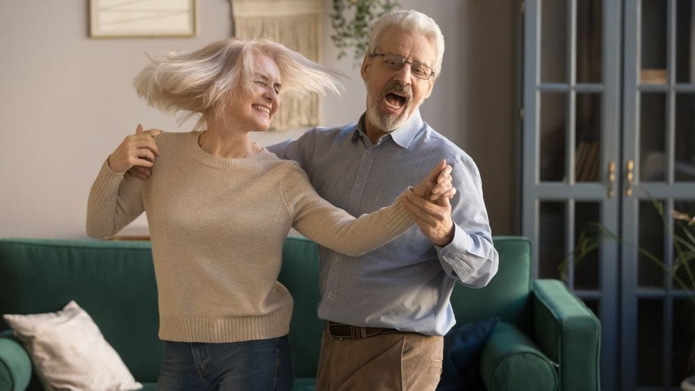 A senior citizen couple dancing in their living room and laughing