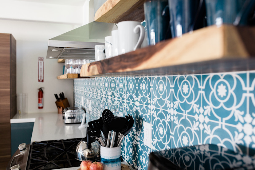 Blue mosaic kitchen backsplash with brass rage hood and open shelving
