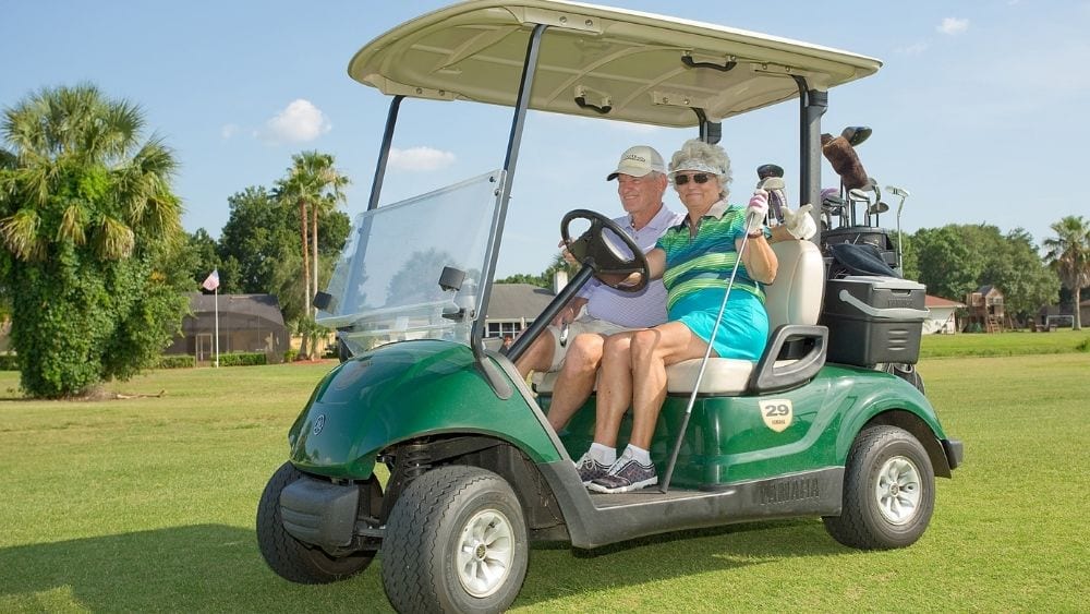 Two active seniors driving a golf cart on golf course.