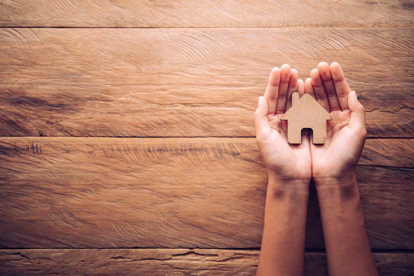 Hands holding a  small wooden model of a house