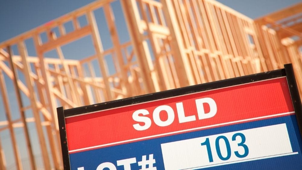 Close up of a “sold” sign in front of the exterior frame of a new home.