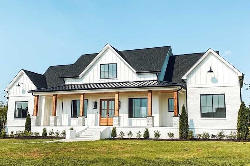 White, traditional farmhouse style home, with black roof, beams on the porch and landscaping