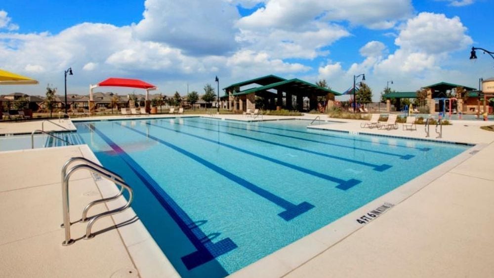 A large pool surrounded by a tiled pool deck with various tanning chairs and awnings surrounding it.
