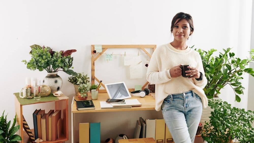 Woman leaning against a wooden desk decorated with plants.