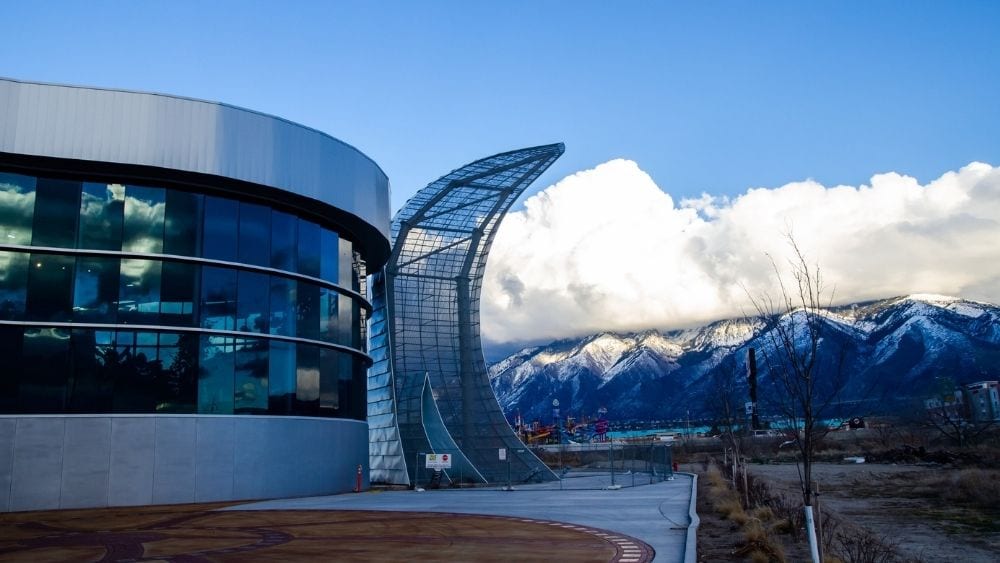 Modern metal and glass city aquarium with mountains and a clear sky in the background.