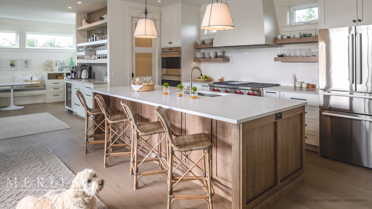 Two-tone kitchen island with stainless steel appliances, a built-in banquette in the background, and a dog lying on the ground, looking at the camera