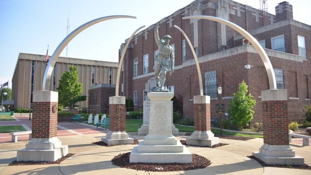 A metal statue of a military member on a white base with curved metal structures around it.