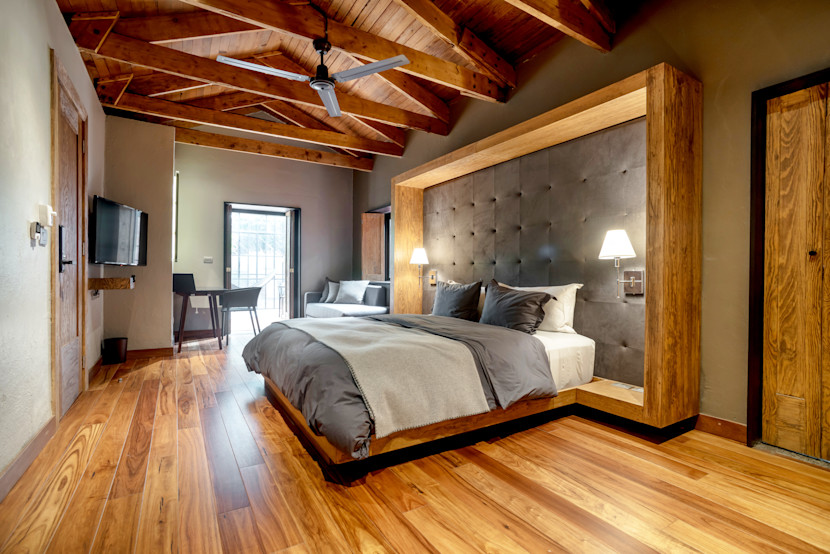 Cozy bedroom with wood ceiling detail , grey tufted headboard and rough hewn log floors