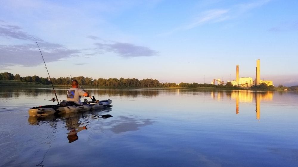 Man kayaking and fishing on a pond.