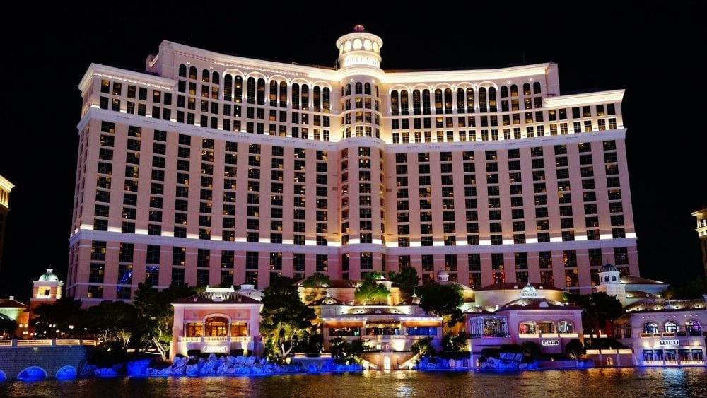 A nighttime shot of an ostentatious hotel with a fountain in the foreground, lit with spotlights.