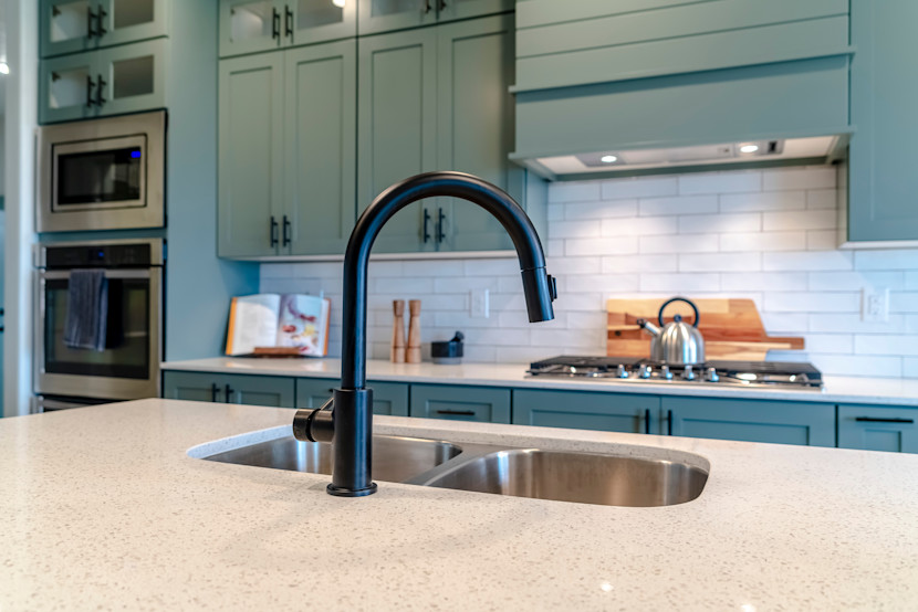 Blue kitchen with gooseneck faucet, custom range hood over a gas stove top, and white subway backsplash