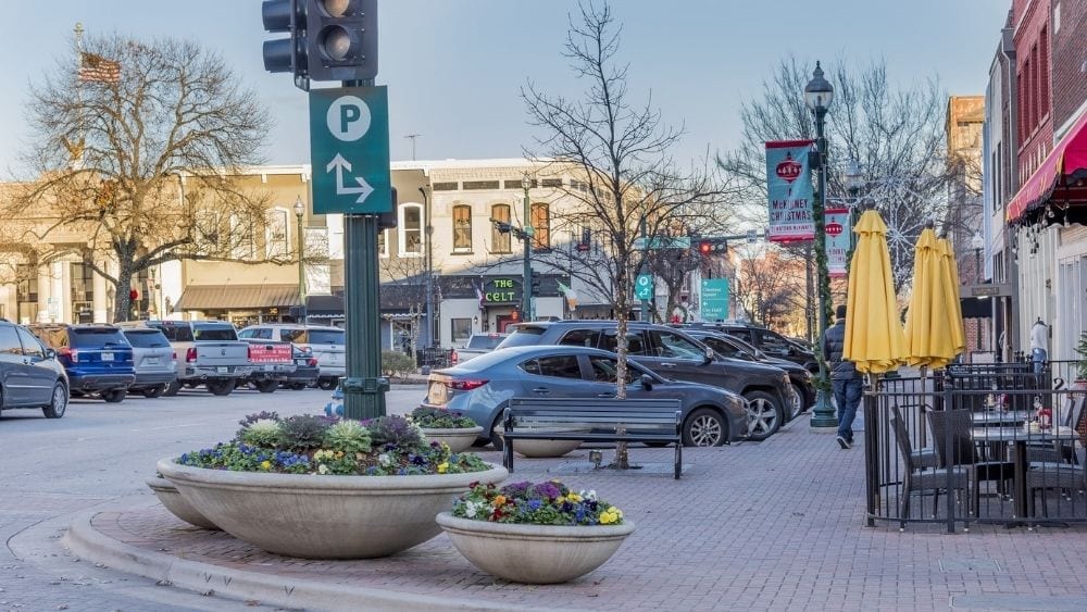 A town square decorated for the holidays with cars parked in every spot.