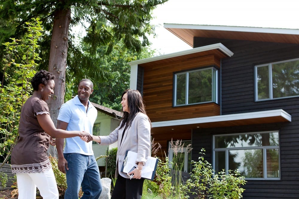 Realtor shaking hands with couple outside of modern home