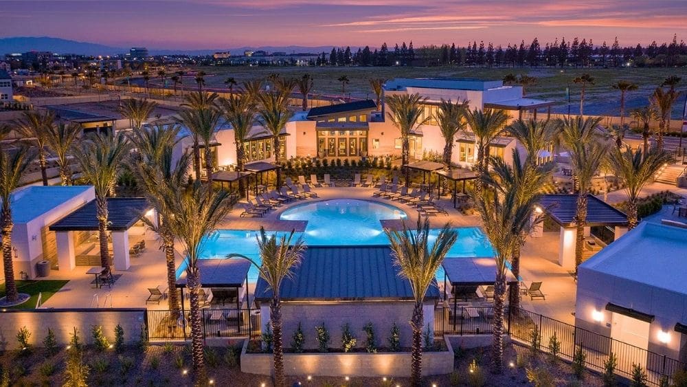 View from above of a grand pool surrounded by palm trees and a Spanish-style building.