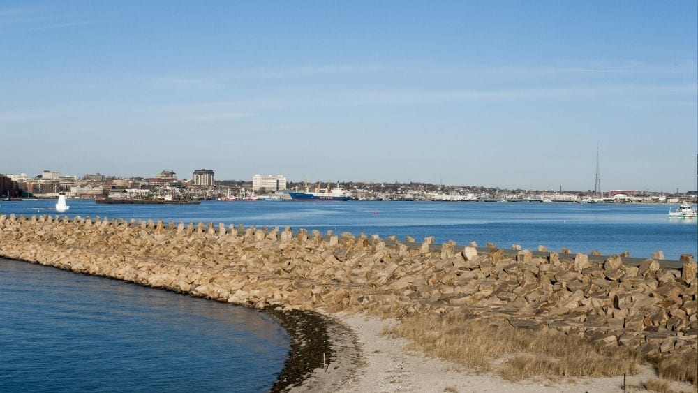 Path of sand and rocks leading out to a city on the water.