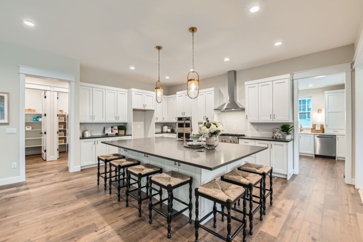 White kitchen with black counter, kitchen island with stool seating on two sides, with extra cabinets in the knee space