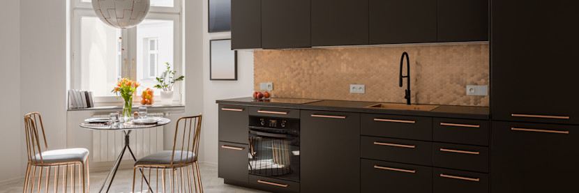 kitchen with black cabinetry and copper fixtures and backsplash, with small dinette table in the corner. 