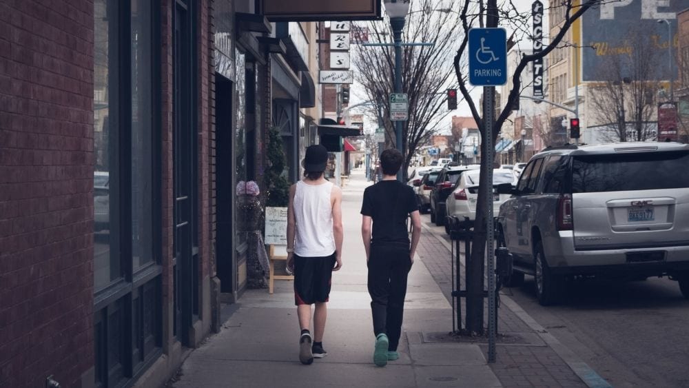 Two people walking down an old-timey street with shops on either side.