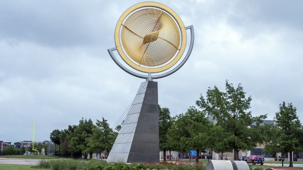 A slanted metal statue with a golden sphere at the top.