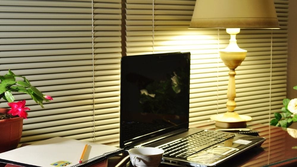 Cluttered desk with a laptop and desk lamp.