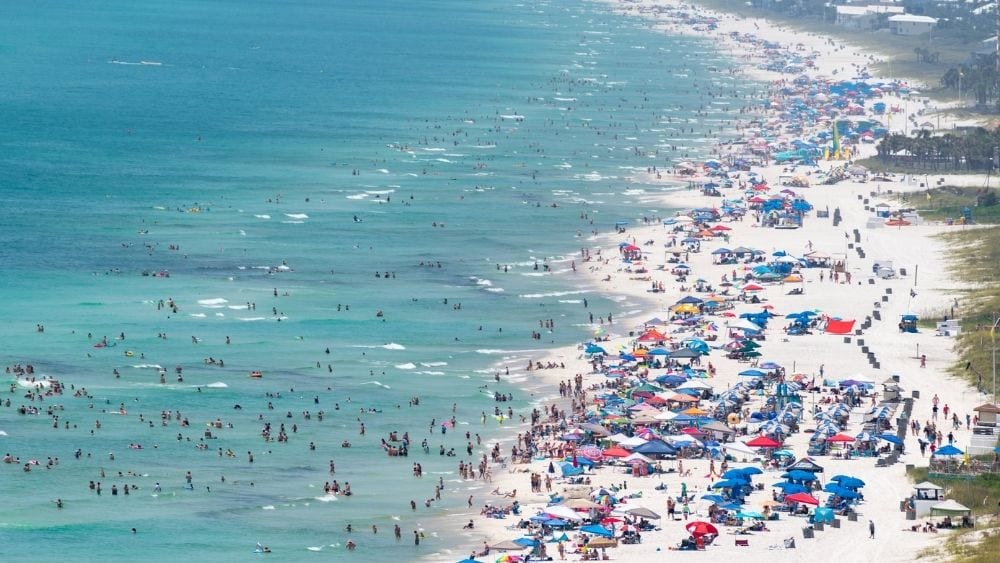 A white sand beach and blue sea packed with visitors.