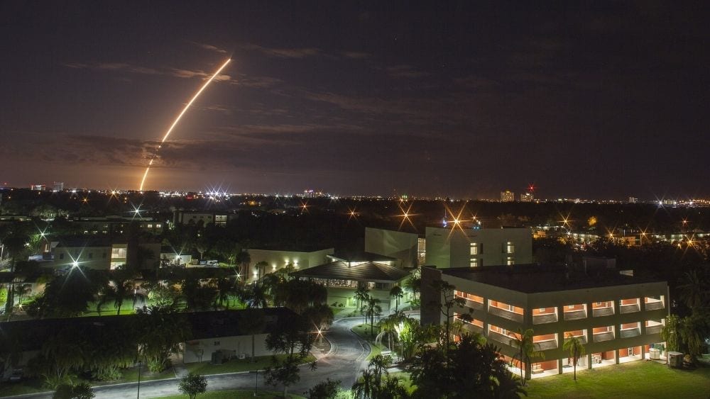 Melbourne at night with a rocket trail slicing through the sky.