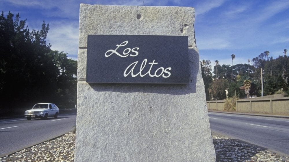 A metal sign etched with “Los Altos” written in cursive and mounted on a stone block.