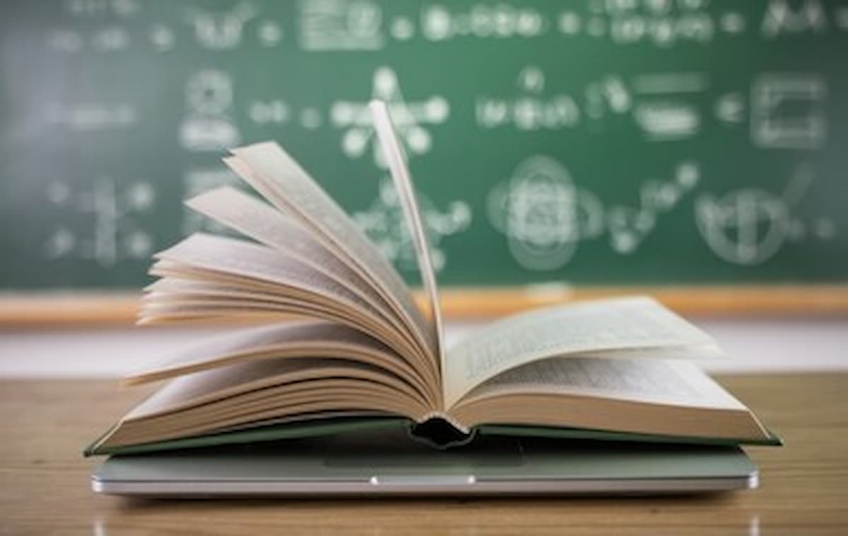book on top of laptop in front of a chalkboard