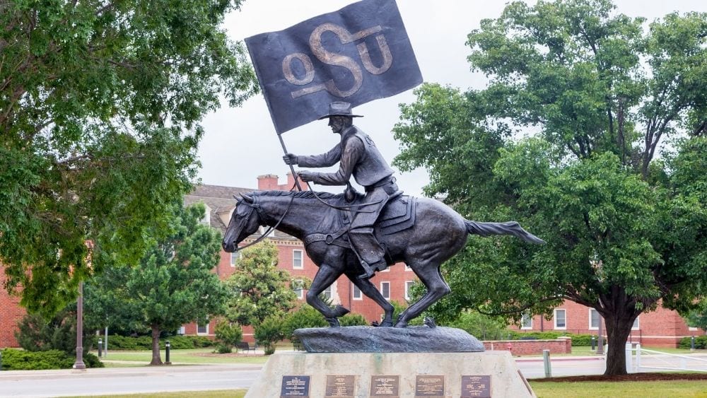 A bronze statue of a man riding a horse, waving an OSU flag.