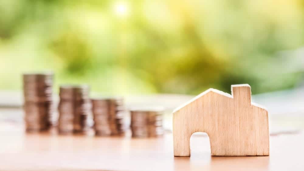 Image of small wooden house in foreground with four stacks of coins in the background