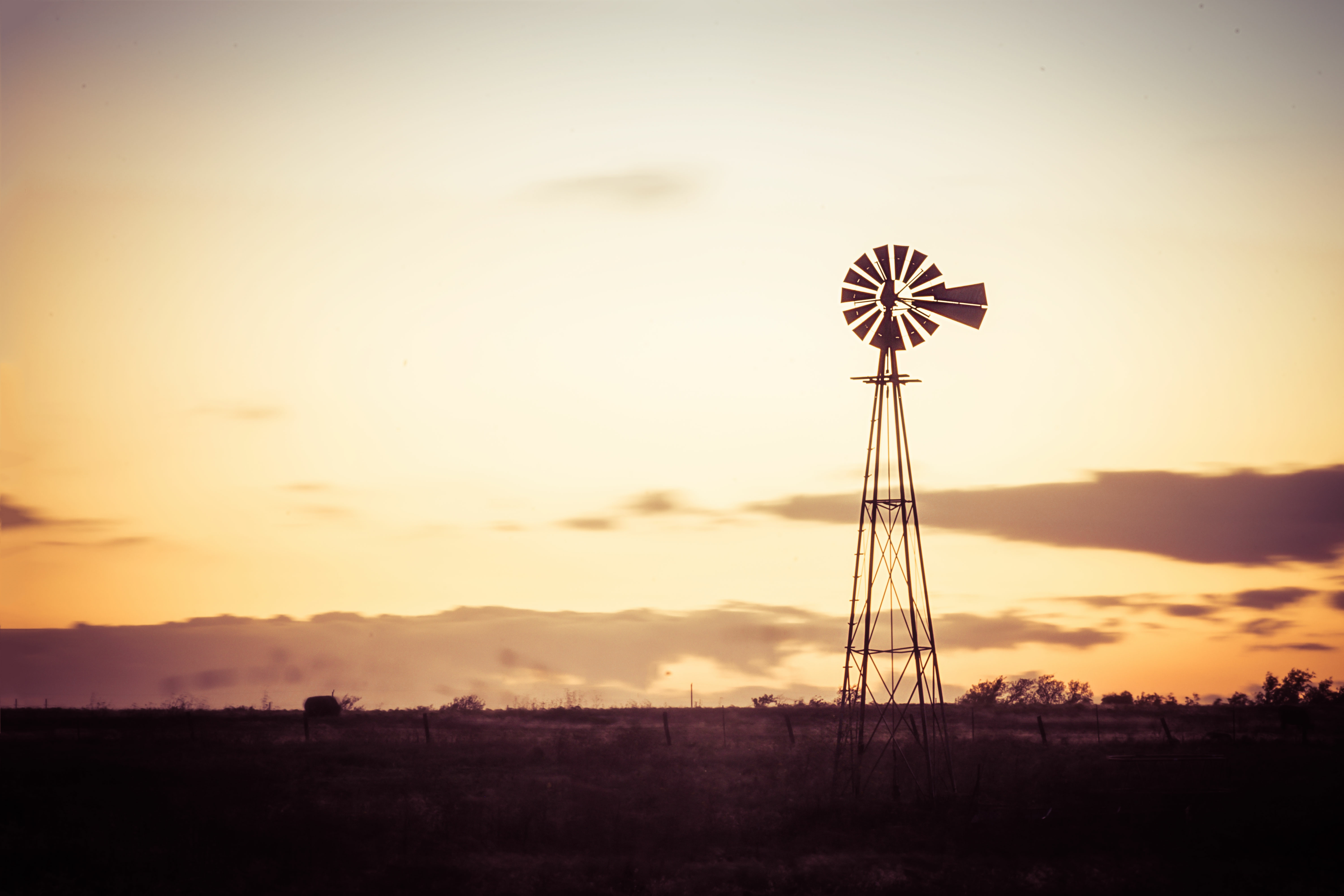 windmill in the foreground of a field against a sunset sky